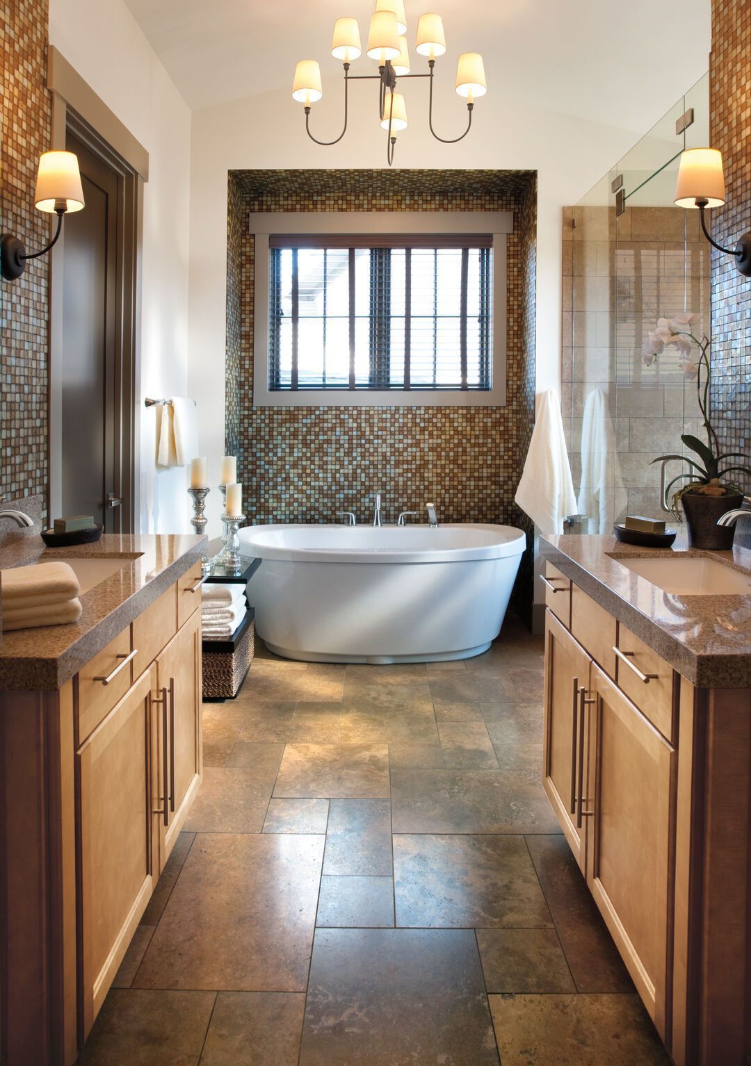 Bathroom with a glass mosaic tiled feature wall, freestanding oval tub, twin maple vanities and travertine tile floor