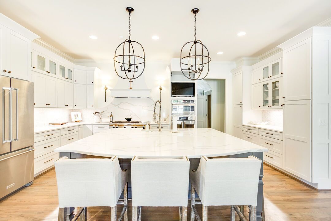 Remodeled white kitchen with a marble-topped island, custom cabinetry and pendant lighting